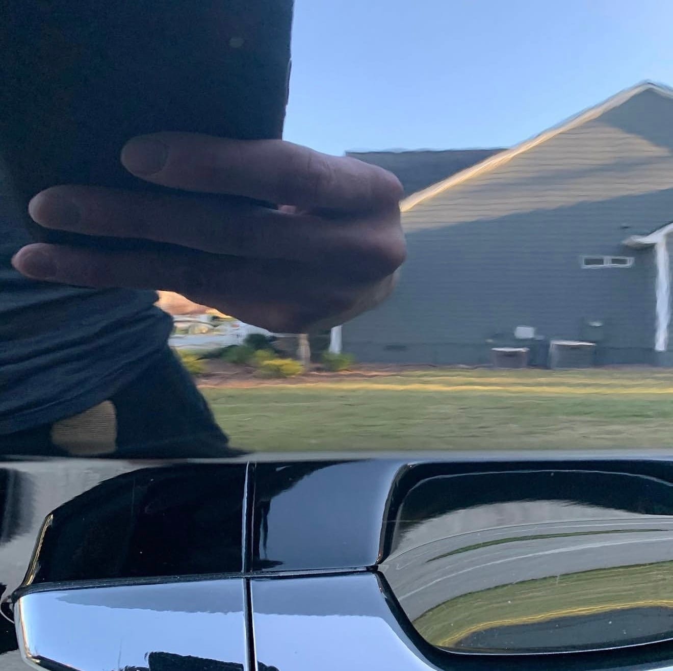 A hand reflected in the glossy black paint of a car door