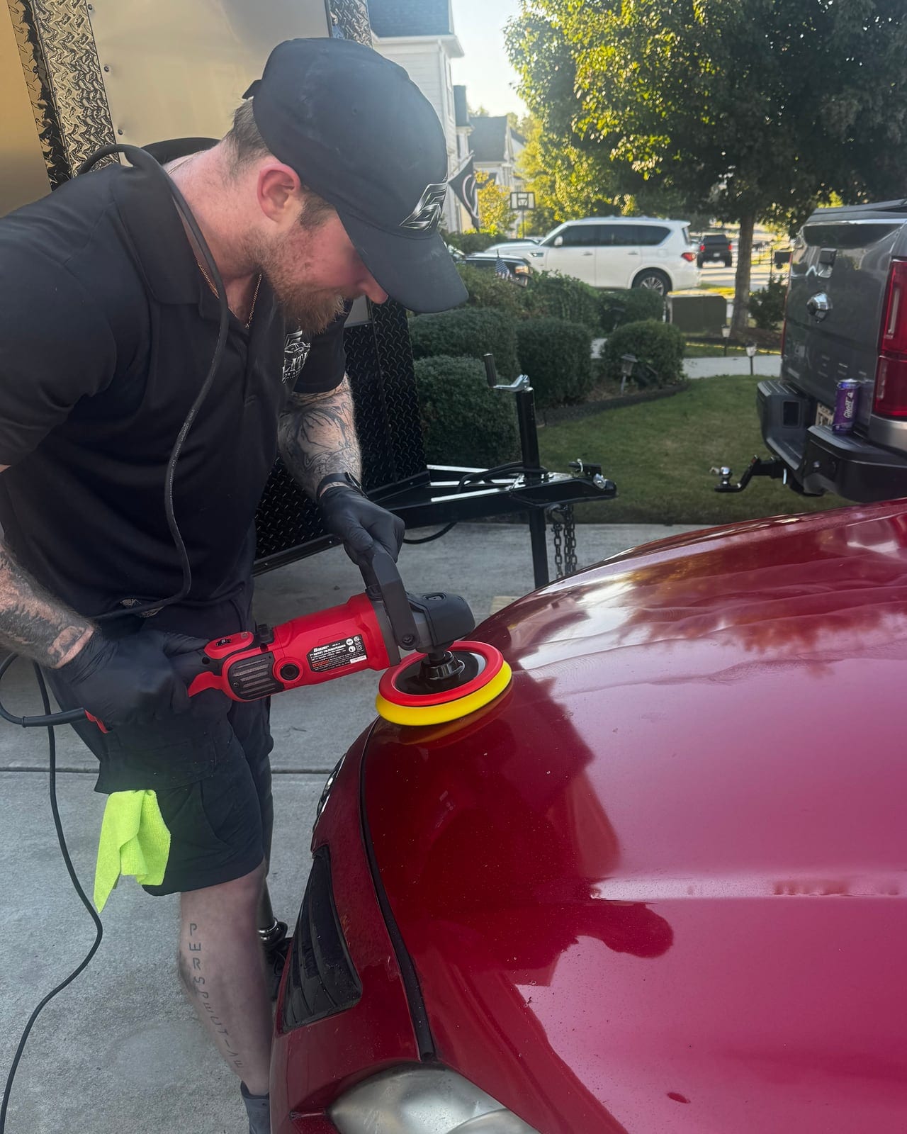 Rob machine-polishing the hood of a red car in a driveway, his trailer behind him